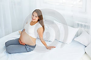 Pregnant Happy smiling Woman sitting on a bed and caressing her