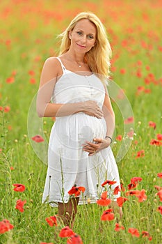 Pregnant happy woman in a flowering poppy field outdoors