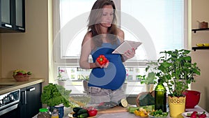 Pregnant housewife holding tablet computer while searching internet for recipe