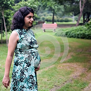 A pregnant Indian lady poses for outdoor pregnancy shoot and hands on belly, Indian pregnant woman puts her hand on her stomach