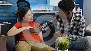 Pregnant interracial couple sitting on sofa at home