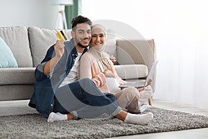 Pregnant Islamic Couple Enjoying Making Online Payments With Laptop And Credit Card