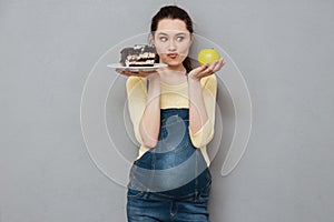 Pregnant lady choosing between sweet cake and apple.