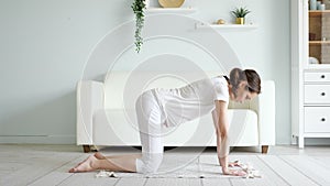 Pregnant lady does marjaryasana on floor near sofa at home