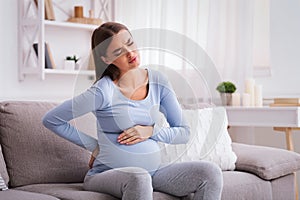 Pregnant Lady Having Backache Massaging Back Sitting On Sofa Indoor