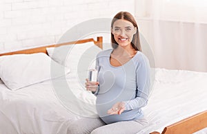 Pregnant Lady Holding Pill And Water Sitting In Bedroom