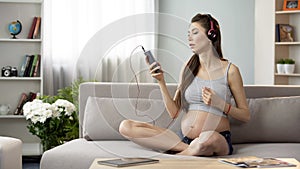 Pregnant lady listening to relaxing music on mobile phone app in headphones