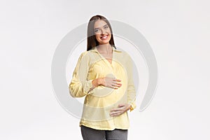 Pregnant Lady Smiling To Camera Touching Belly Over White Background