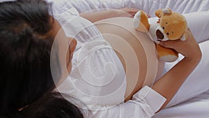 Pregnant latin american woman sitting in couch holding and moving teddy bear close to her stomach