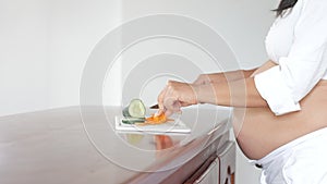 Pregnant Latin American woman standing at wood counter in kitchen cutting vegetables