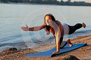 Pregnant mid adult woman exercising on a beach at sunset