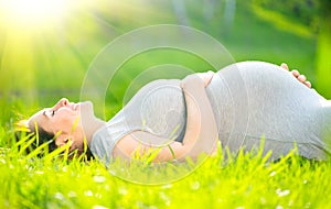 Pregnant middle aged woman touching her belly lying on green grass, enjoying nature. Pregnancy concept