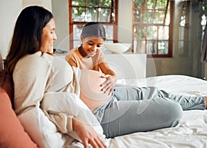 Pregnant mom and curious child on bed touching belly with excited, happy and joyful smile. Indian family and kid waiting