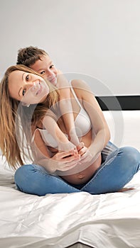 Pregnant mom talking and playing with her child in the bedroom. Mother with son sharing good emotions while relaxing at