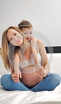 Pregnant mom talking and playing with her child in the bedroom. Mother with son sharing good emotions while relaxing at