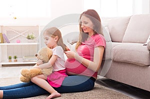 Pregnant mother combing her daughter at home
