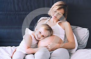 Pregnant mother and daughter resting in bed. Young woman with her first child during second pregnancy. Motherhood and parenting