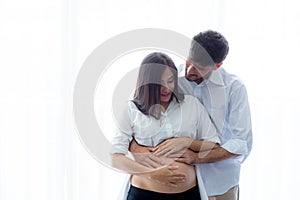 Pregnant Mother and father standing hugging holding belly.