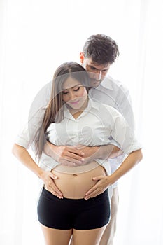 Pregnant Mother and father standing hugging holding belly heart shape with hand