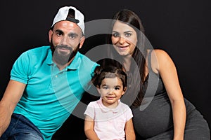 Pregnant mother with her family sit on floor black background