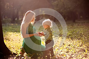 Pregnant mother and her little son in the park at sunset