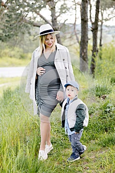 Pregnant mother and her little son walking in the forest and spending time together