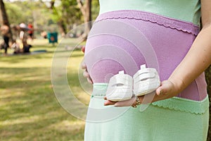 Pregnant mother holding newborn baby's bootie in a park.