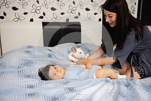 Pregnant Mother laying with her baby son on the bedroom bed playing and having fun - Asian mixed ethnicity child Boy