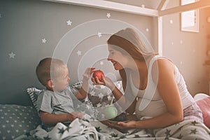 Pregnant mother and little boy son are eating an apple and peach in the bed t home in the morning. Casual lifestyle in