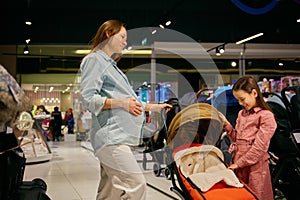 Pregnant mother and little daughter choosing stroller in shopping mall