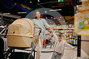 Pregnant mother and little son selecting pram for new family member in store