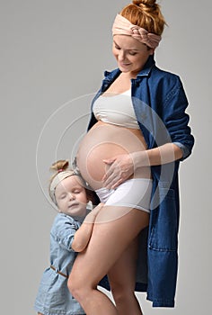 Pregnant mother and lovely daughter touching mother`s pregnant belly. Happy little girl feeling baby at mother tummy