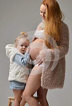 Pregnant mother and lovely daughter touching mother`s pregnant belly. Happy little girl feeling baby at mother tummy