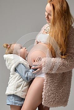 Pregnant mother and lovely daughter touching mother`s pregnant belly. Happy little girl feeling baby at mother tummy