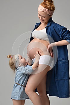 Pregnant mother and lovely daughter touching mothers pregnant belly. Happy little girl feeling baby at mother tummy