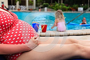 Pregnant mother relax by the pool while kids play with water