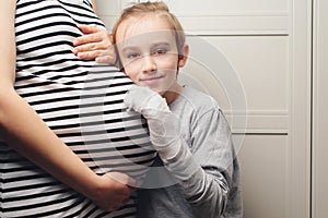 Pregnant mother and son at home. Cute boy with mom spending time together at home. Child boy hugging his mother pregnant tummy