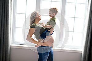 A Pregnant mother and son spending time together in bedroom close to the window