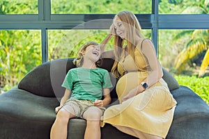 Pregnant mother and son are talking and spending time together at home. Little child boy looking at her mother pregnant