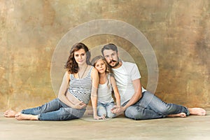 Pregnant mother with teen daughter and husband. Family studio portrait over brown background