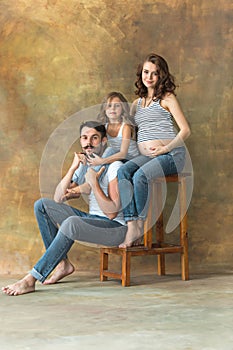 Pregnant mother with teen daughter and husband. Family studio portrait over brown background