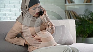 Pregnant muslim female feeling pain, calling emergency smartphone, contractions