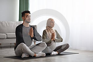 Pregnant Muslim Woman In Hijab Meditating Together With Her Husband At Home