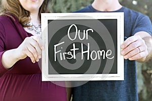 Pregnant new family buying their new home holding our first home sign