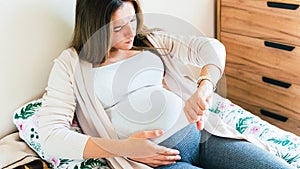 Pregnant pain contractions. Pregnant woman watching clock, holding baby belly. Childbirth time, contractions pain