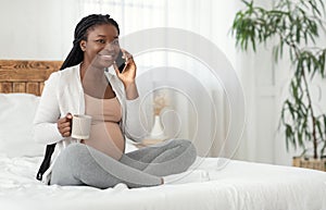 Pregnant Pastime. Smiling Black Expectant Mother Talking On Cellphone And Drinking Tea