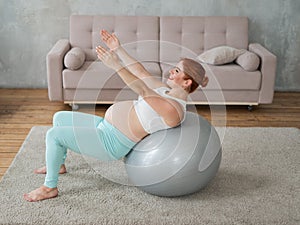 Pregnant red-haired woman doing exercises on fitness ball at home.