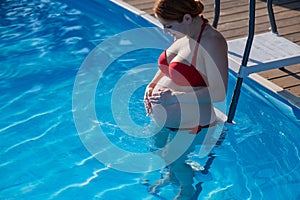 Pregnant red-haired woman in the pool in a red bikini.