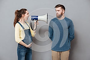 Pregnant screaming woman holding loudspeaker near serious man