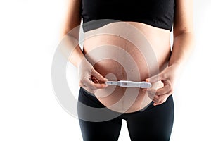 Pregnant skinny slim fit woman holding a positive pregnancy test on her belly tummy abdomen